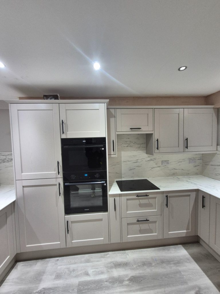 Riva shaker cabinetry with tall appliance housing, black ovens, an induction hob and light compact laminate surfaces.