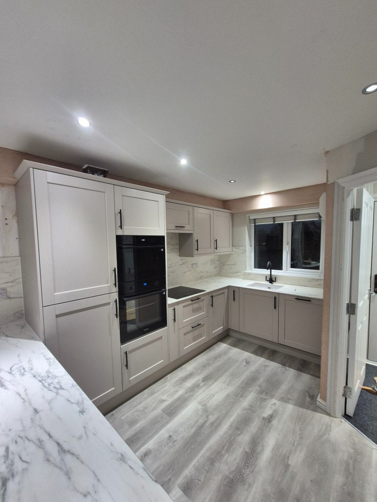 Completed Riva shaker kitchen with light worktops, matching marble-effect splashbacks, black handles and LVT flooring.