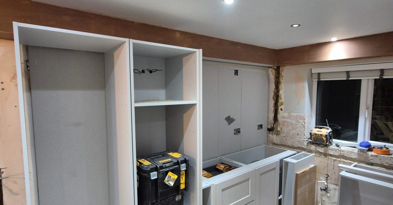 New shaker kitchen cabinets being installed against prepared walls with the original floor covering removed.
