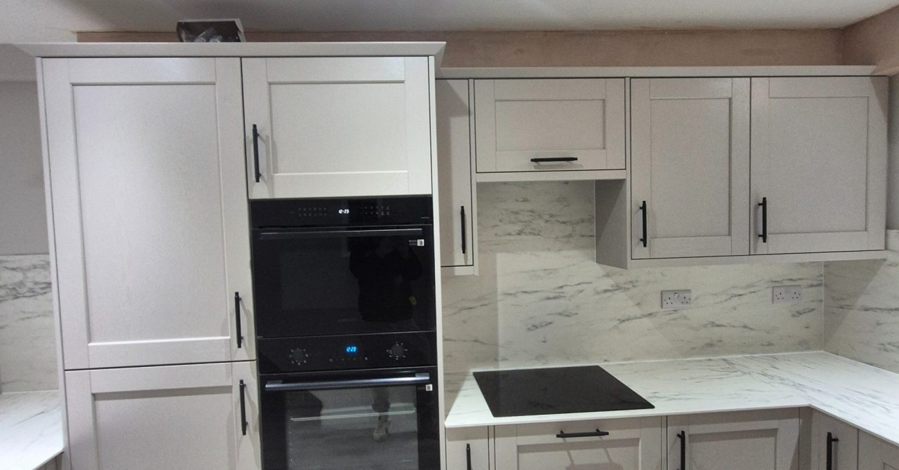 Riva shaker cabinetry with tall appliance housing, black ovens, an induction hob and light compact laminate surfaces.