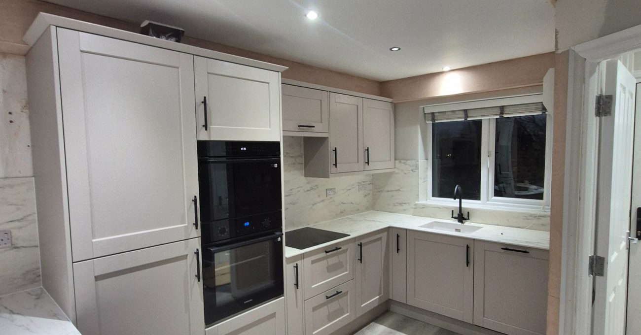 Completed Riva shaker kitchen with light worktops, matching marble-effect splashbacks, black handles and LVT flooring.