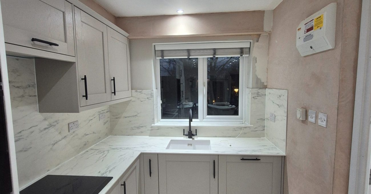Wide view of the completed Stamford kitchen showing shaker cabinets, integrated appliances, light surfaces and grey LVT flooring.
